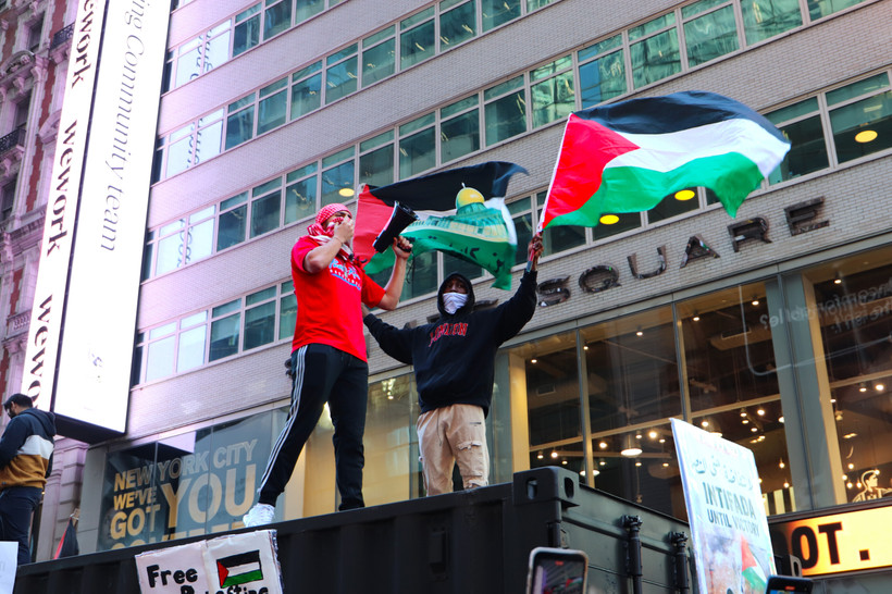 Two on a platform fly Palestinian flags and hold a megaphone in Times Square.