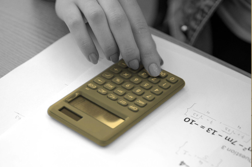 A student's hand using a calculator on a math worksheet.