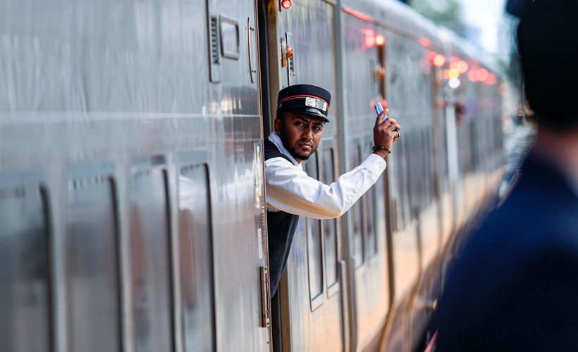 A Long Island Rail Road conductor stands on a train and gestures with his hand.