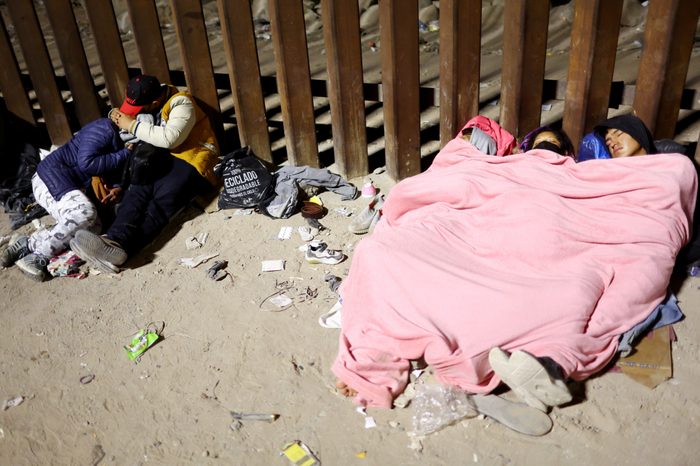 Immigrants sleep against the U.S.-Mexico border barrier in the early morning hours as they wait to be processed by U.S. Border Patrol.