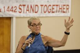Jane McAlevey addresses a crowd before a banner that reads in part "STAND TOGETHER."