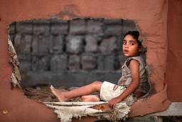 A child sits sideways looking through a torn canvas wall.