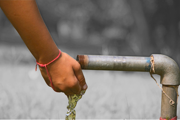 Someone rinses their hand with water from a rusty lead pipe in a park.