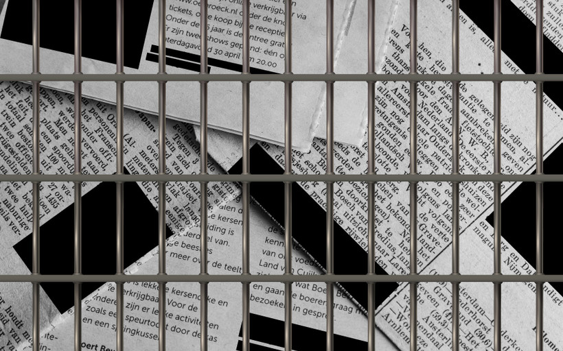 a stack of newspapers, with redaction boxes covering the text, behind prison bars