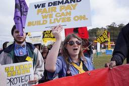 Woman in sunglasses and Waffle House uniform holds a sign reading "We Demand Fair Pay We Can Build Lives On" with marchers behind her