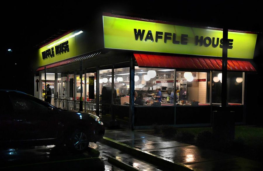 Waffle House yellow sign in rainy darkness. Lit up inside are customers and a server.