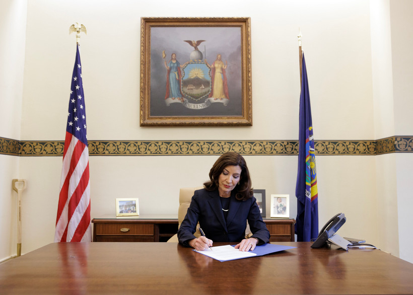 New York Governor Kathy Hochul sits at a large wooden table and signs papers in Albany, New York.