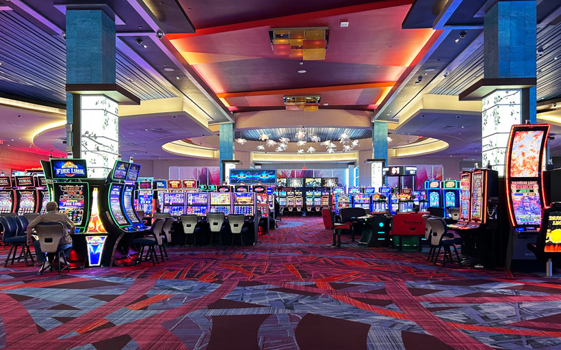 Photo of a casino floor with rows of brightly lit video lottery terminals and a single player sitting to the left in front of a terminal.