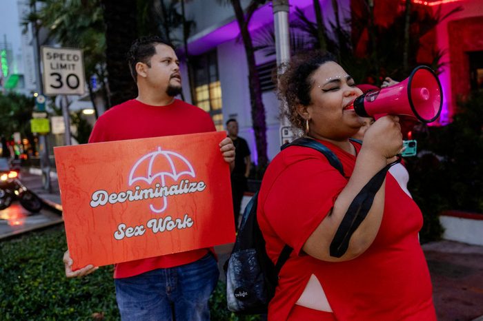 A woman calls through a bullhorn; a man holds a sign that reads "Decriminalize Sex Work"