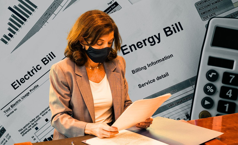 Hochul reading a piece of paper against the backdrop of energy bills