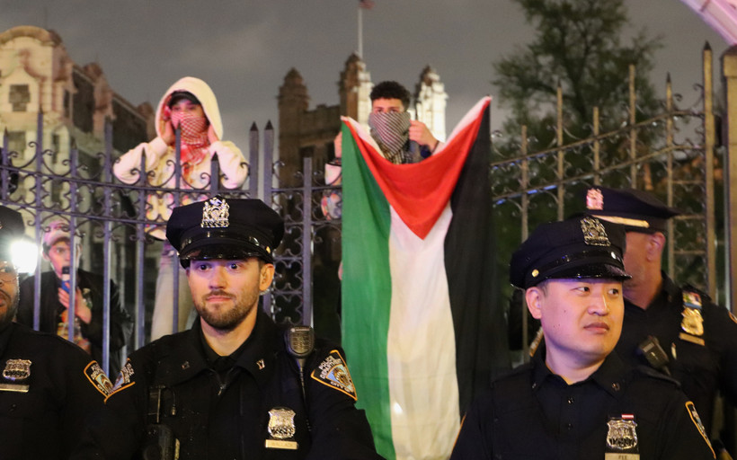 NYPD officers in front of the City College gates. Protesters drop a Palestinian flag behind them.