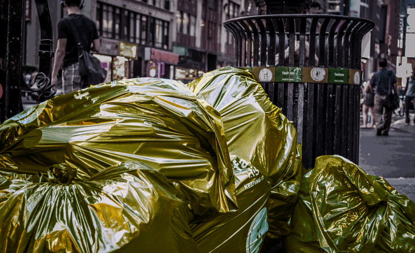 Bags of trash with a golden filter sit in front of a trash can on the curb in New York City