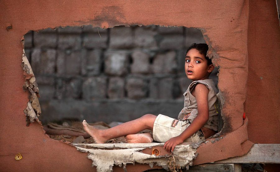 A child sits sideways looking through a torn canvas wall.