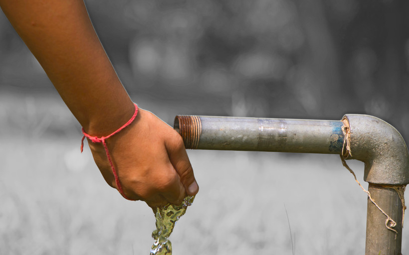 Someone rinses their hand with water from a rusty lead pipe in a park.