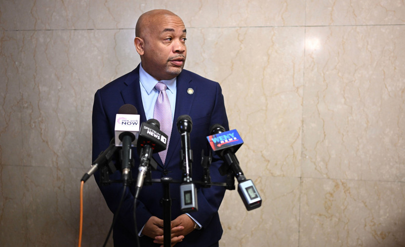 New York State Assembly speaker Carl Heastie stands in front of a tile wall with TV microphones.