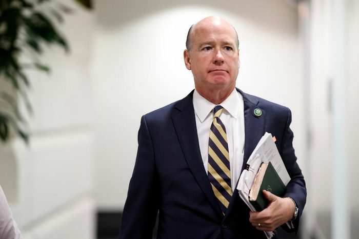 Robert Aderholt walks down a hallway in a suit and tie with papers under his arm.