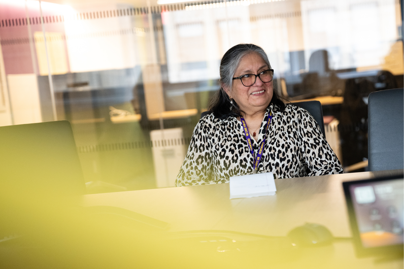 Bertha Motta sits smiling at a desk, wearing an 1199 SEU lanyard.