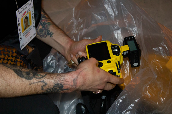 hands holding yellow camera in a plastic trash bag, press badge visible
