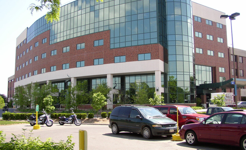 Exterior of a hospital with cars and motorcycles parked in front