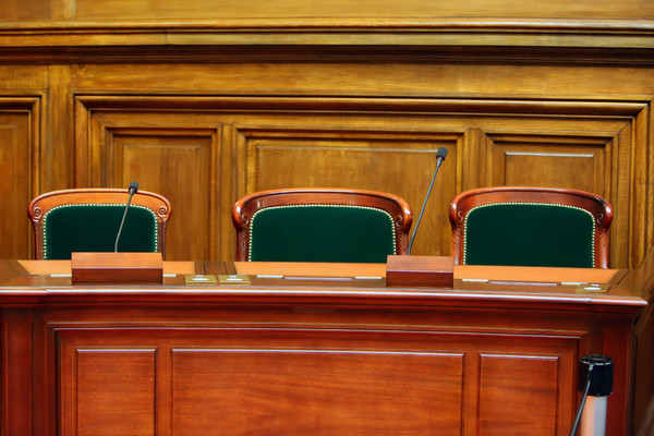 Three empty seats inside of a wood-paneled hearing room.