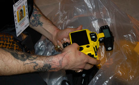 hands holding yellow camera in a plastic trash bag, press badge visible