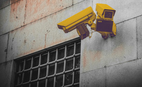 Photo of a prison wall with barred windows and two yellow security cameras pointing outwards.