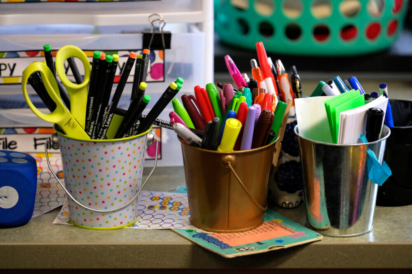 Three small pails sit atop a counter, one filled with pencils, another filled with markers, and another filled with sticky notes.