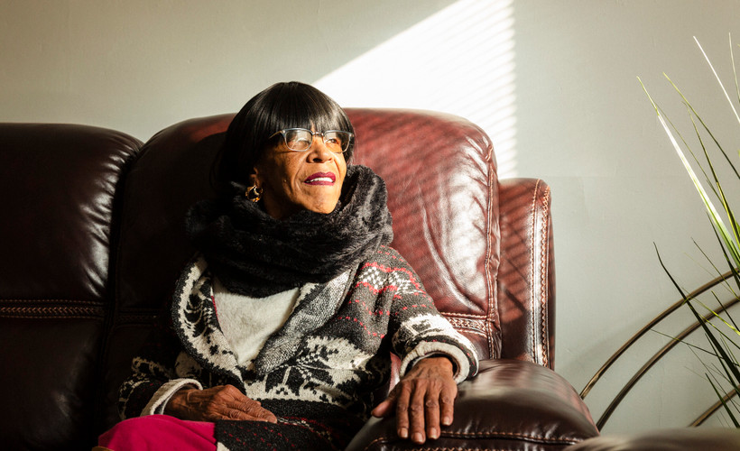 Sunlight illuminates Renay Lynch's smiling face as she sits on a leather couch next to the window.