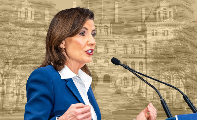 A photo collage of Governor Kathy Hochul over a yellow-tinted photo of many tall stacks of paper superimposed onto the New York state Capitol.