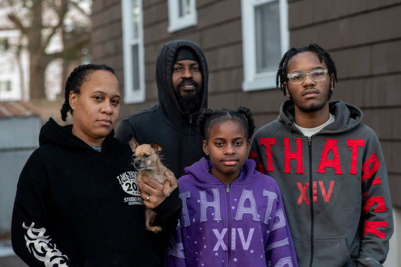 The Stradford-Moses family stands outside its home. Jasmine Stradford holds one of the family’s dogs in her hand.