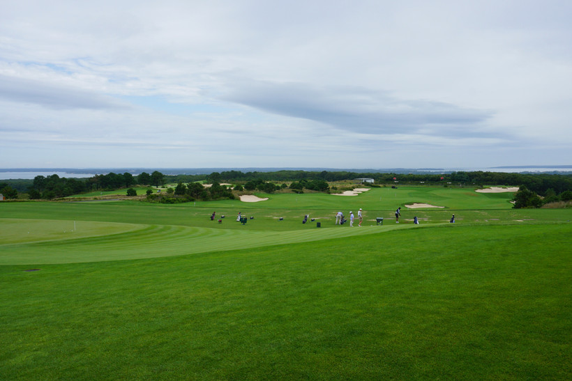 Golfers on an expansive green field under a blue-gray sky.