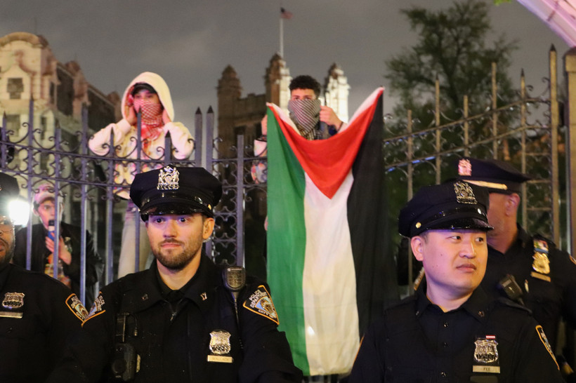 NYPD officers in front of the City College gates. Protesters drop a Palestinian flag behind them.