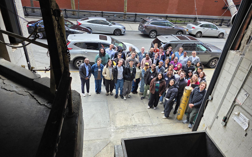 A group of about 50 people pose for a photo taken from inside a garage housing a trash compactor.