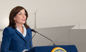 Photo montage showing NY Governor Kathy Hochul speaking on April 28 against a greyed-out backdrop of solar panels and a wind turbine.