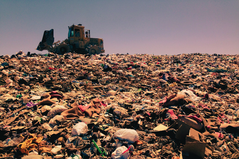A bulldozer sits on top of a landfill full of trash.