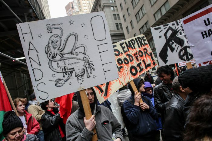Protesters walk through the streets of New York with signs saying "No U.S. empire No blood for oil" and depicting the United States as an octopus strangling Venezuela.
