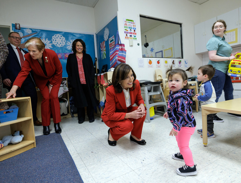 New York governor Kathy Hochul kneels in a red suit with a child looking out in distress
