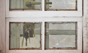 A jail cell with keys in the lock seen through a dirty window.