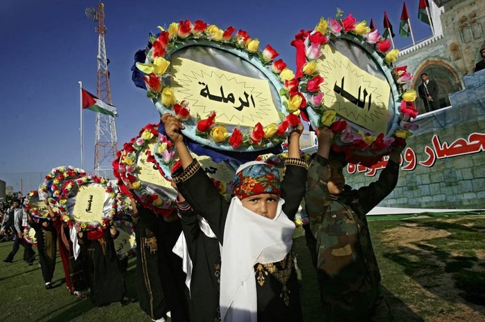 A line of children hold above their heads circular flower garlands with text in Arabic written inside.