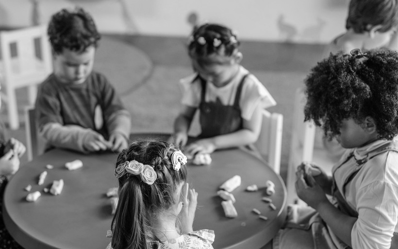 Four young children sit around a table, playing with clay.