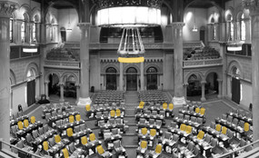 A black and white photo of the state Assembly chamber with yellow highlighting several empty seats.