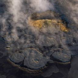 Mist rises over a barren landscape with a single green patch