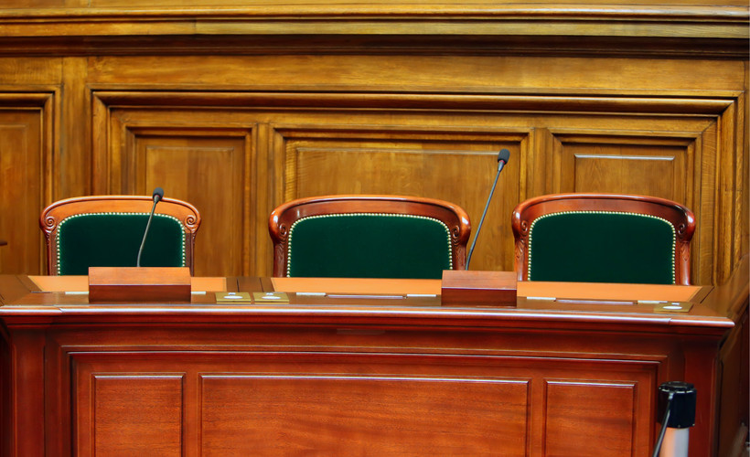 Three empty seats inside of a wood-paneled hearing room.