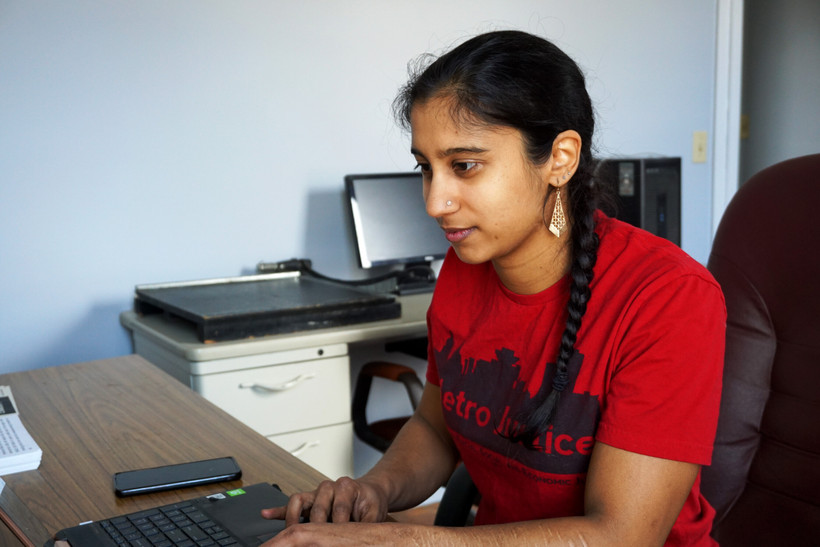 Mohini Sharma sits at a computer wearing a red Metro Justice t-shirt.