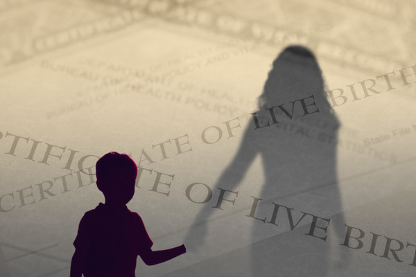 A child silhouetted in the foreground holds hands with an adult, who is separated from the child by a transparent layer composed of birth certificate paperwork.