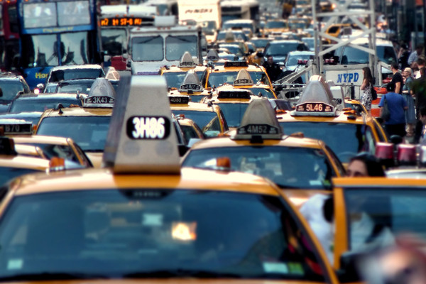 The image depicts a traffic jam in New York City, with a cluster of yellow taxi cabs at the front.