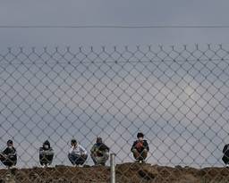 Six people crouching behind a wire fence