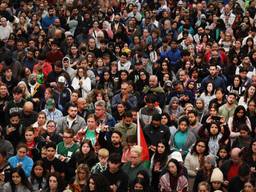 Hundreds of people of different backgrounds stand shoulder to shoulder in a crowd.