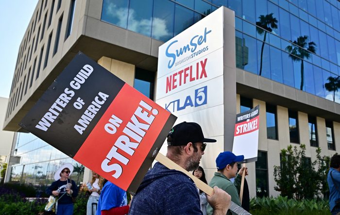 Someone holds a sign on a wooden stick that reads, "Writers Guild of America on Strike!" while picketing with others in front of Netflix in Hollywood, Calif.