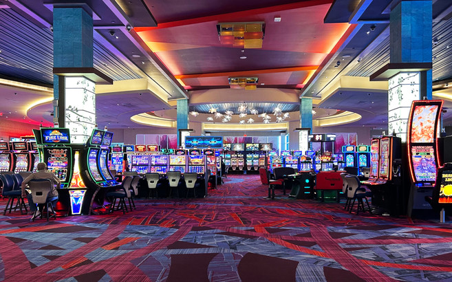 Photo of a casino floor with rows of brightly lit video lottery terminals and a single player sitting to the left in front of a terminal.
